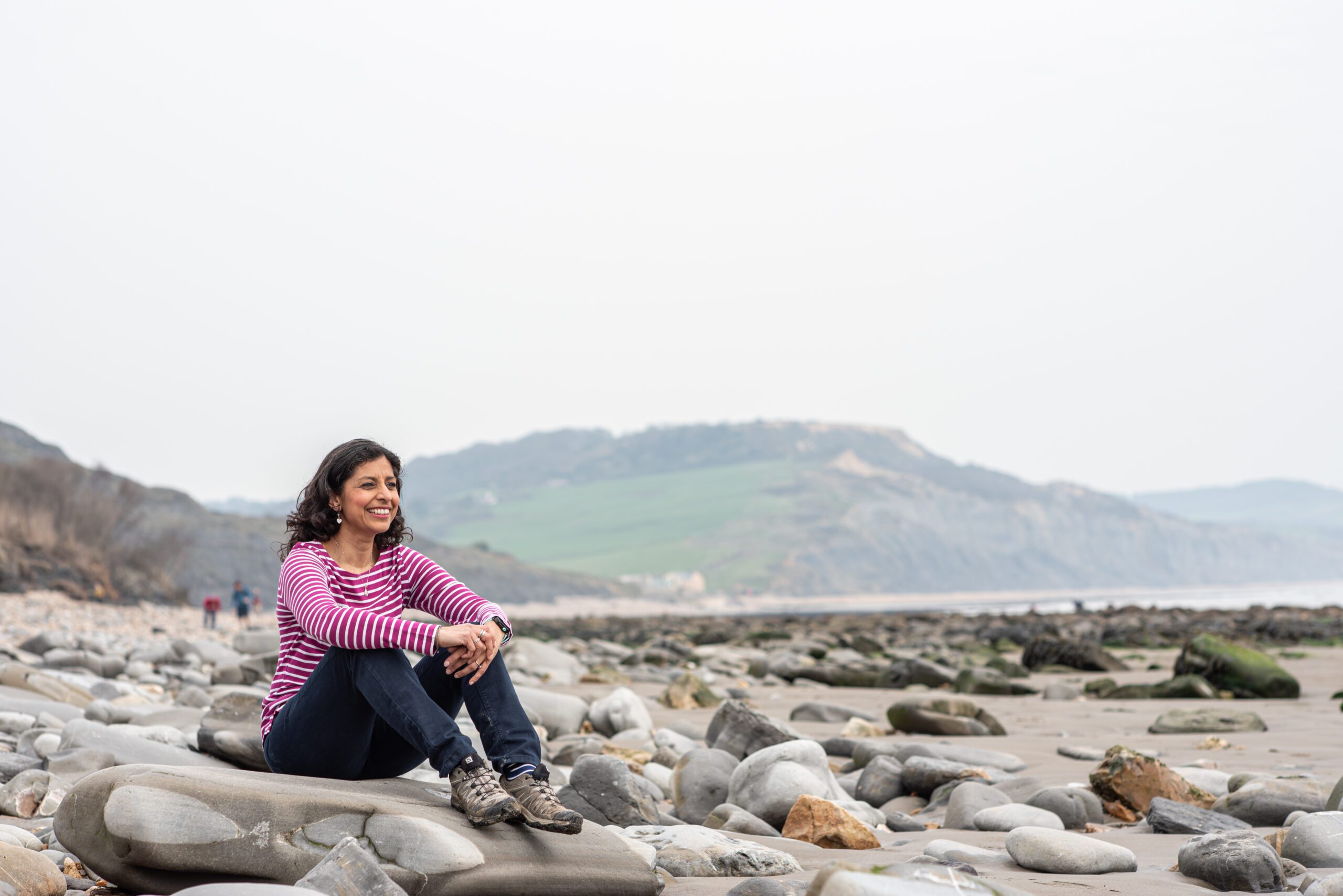 Dr Anjana Khatwa sits on stones by the sea.