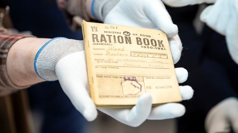 A ration book from the MERL collections being held by a staff member wearing white gloves