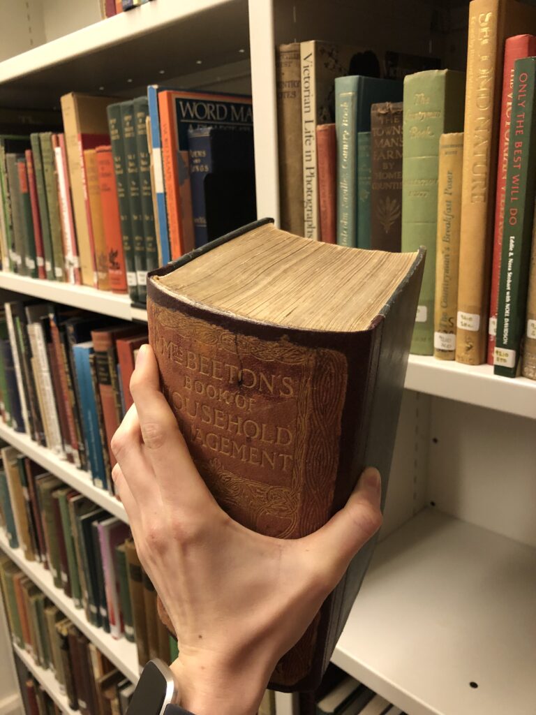 A person holds a copy of Mrs Beeton's Book of Household Management.