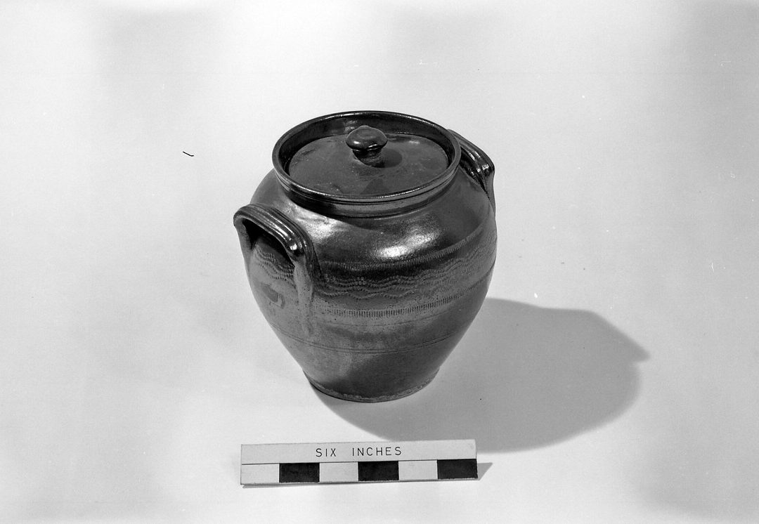 This is a brown stoneware jar and a lid, which was used for storing food.