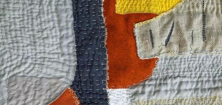 Details of a quilt made out from grey, blue, orange, yellow and white material