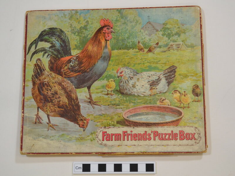 This thick card jigsaw puzzle has four puzzles, each with 12 pieces. The puzzles depict; a cockerel and two hens with chicks (on the lid); sheep and lambs; ducks on a pond; horse and foals with a girl on a toy horse with a dog. The puzzle is by Ernest Nister. This is one of a large collection of jigsaw puzzles on a rural theme complied by a private collector.