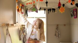 A girl reaching up to touch the knitted decorations in the shepherd's hut in the MERL garden