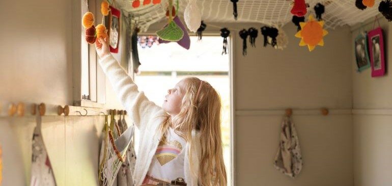 A girl reaching up to touch the knitted decorations in the shepherd's hut in the MERL garden