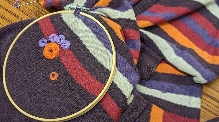part of a recycled garment in an embroidery hoop with flowers being sewn on
