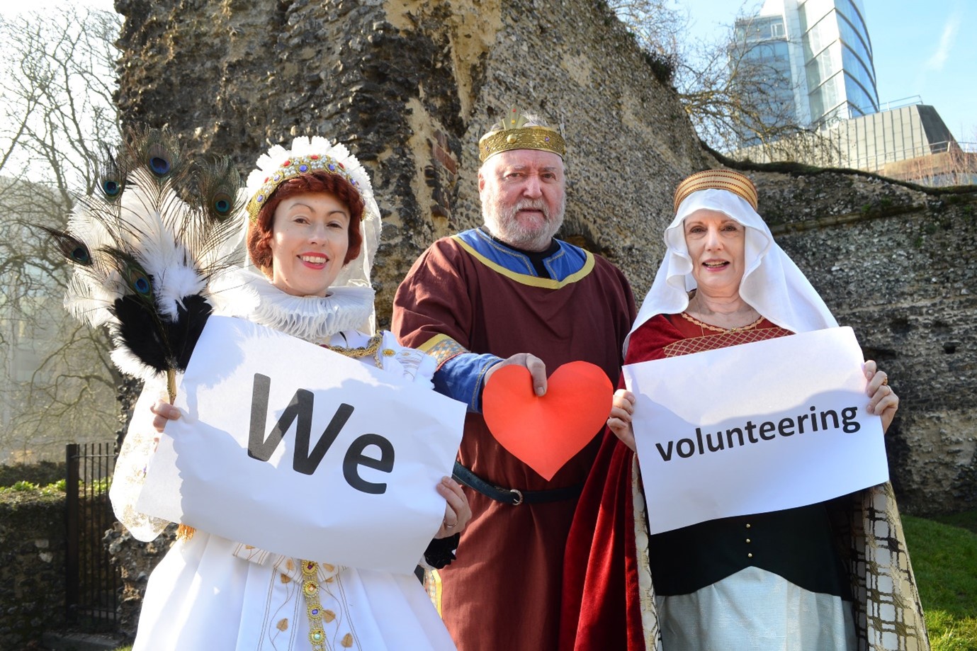 Three costumed interpreters are holding up pieces of paper which spell out ‘We Love Volunteering’. From left to right: Queen Elizabeth I, King Henry I and Empress Matilda.