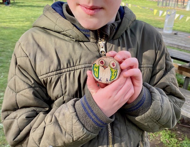 a child holding up a piece of wood decorated as an owl