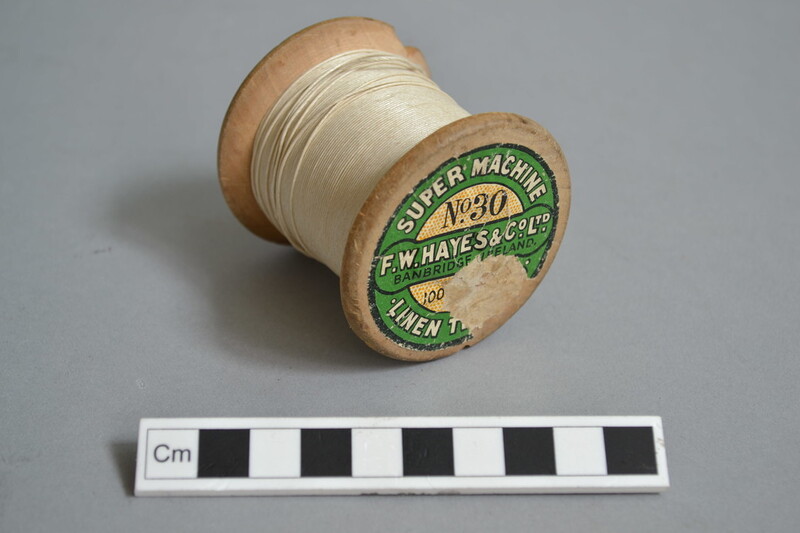 A large bobbin, with cream coloured thread and a green label