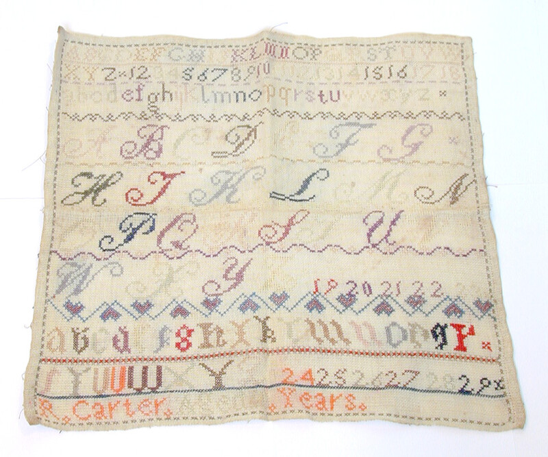 A needlework sampler features the alphabet in lower case, cursive and block capitals. The letters come in multiple colours, some are now more faded than others.