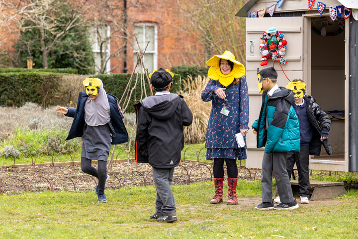School children enjoying a create a buzz activity in the MERL garden, with a member of staff wearing a large daffodil head dress