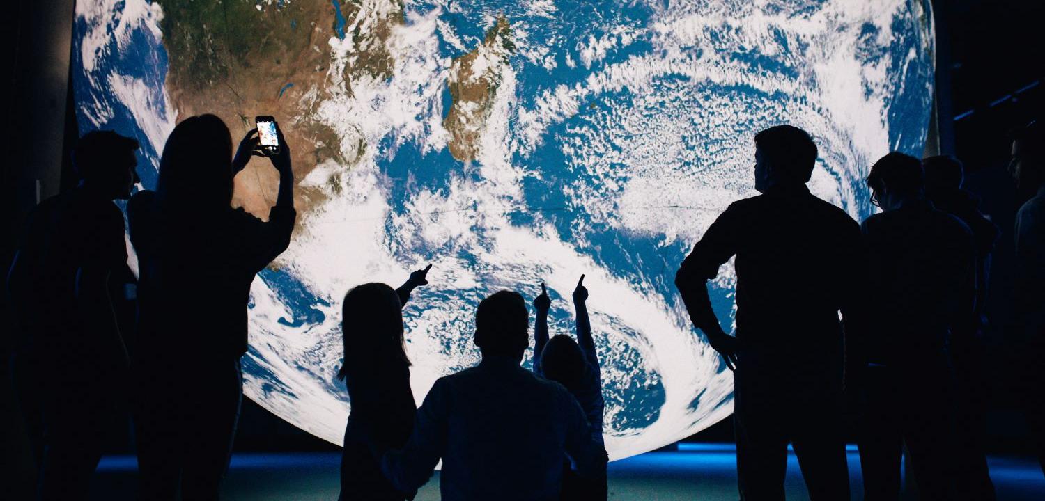 silhouettes of people standing in front of a large image of teh earth