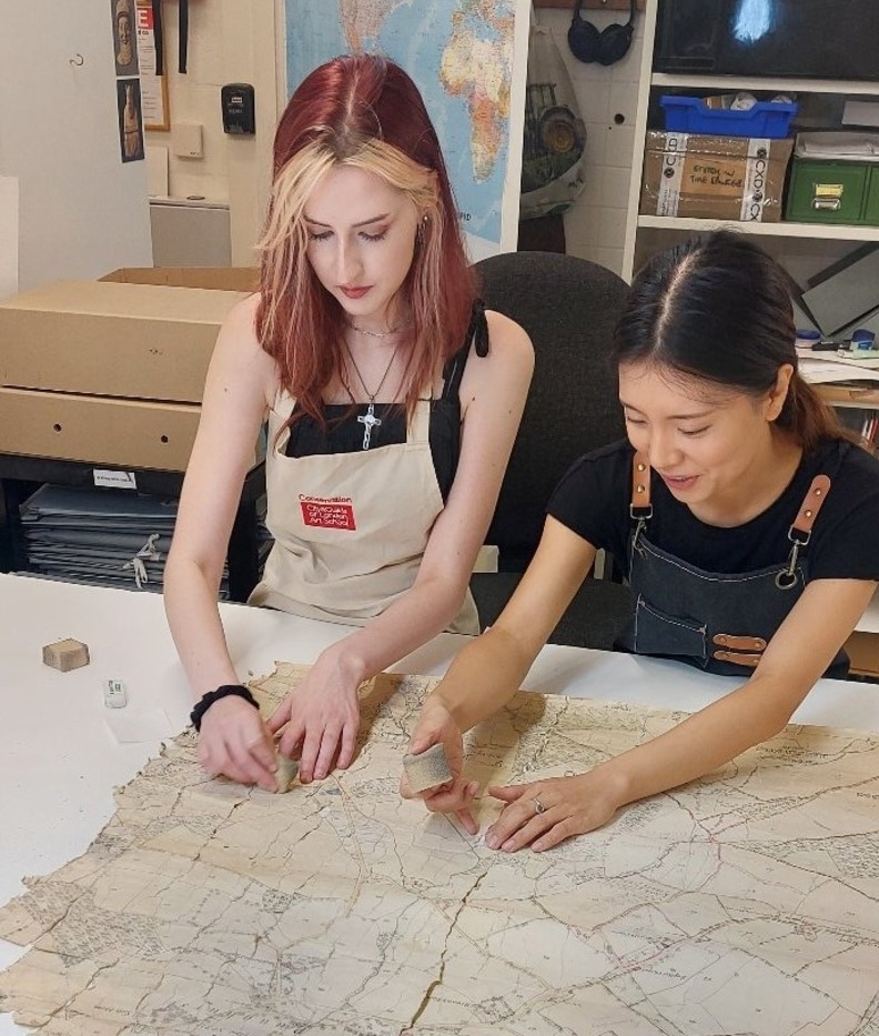 Trainees using latex sponges to clean the surface dirt from one half of a large format Wellington Estate Map.