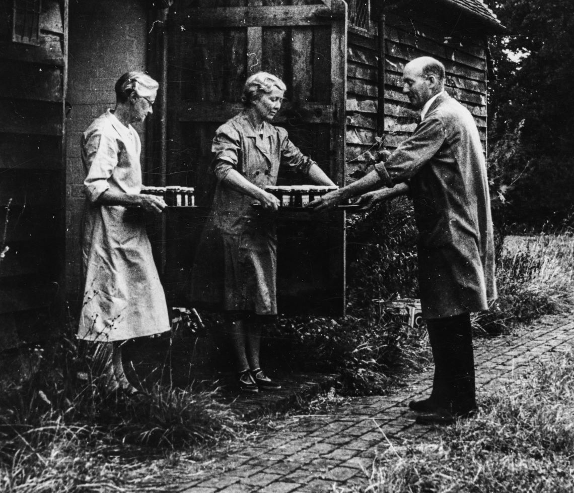 Black and white photograph of two women handing jam to a man
