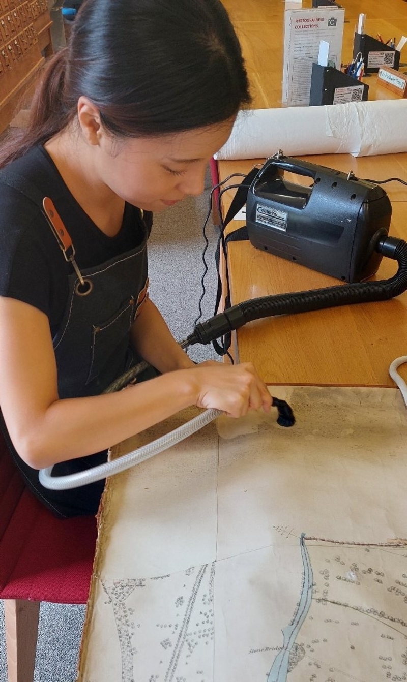 One of the interns vacuuming the loose surface dirt from one of the large format rolled maps in the Wellington Estate archive.