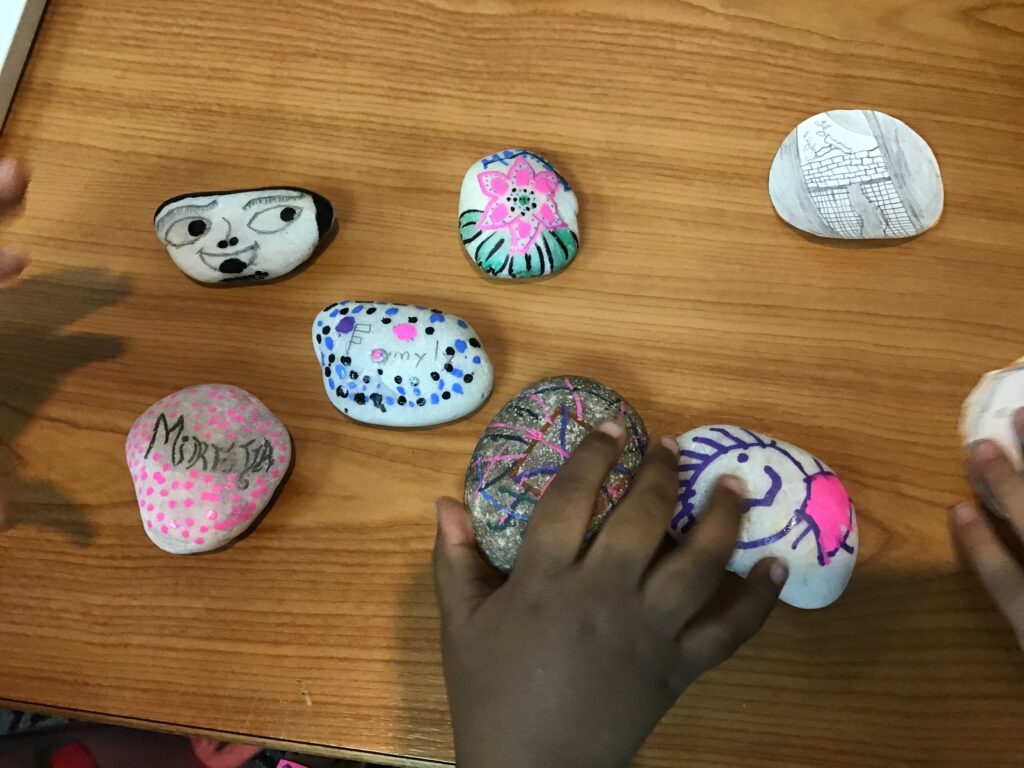 a child's hand picking up a painted rock