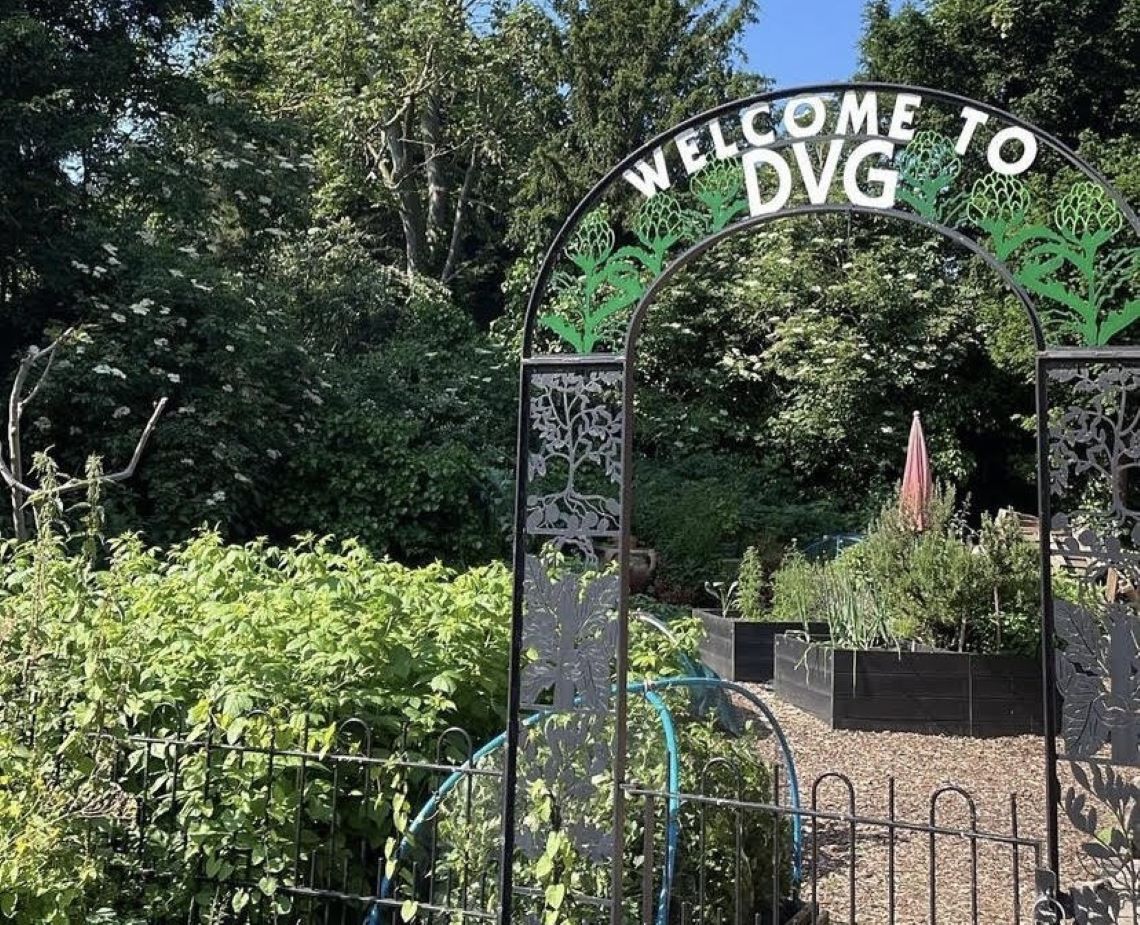 A gateway with a sign reading "Welcome to DVG" with a garden behind