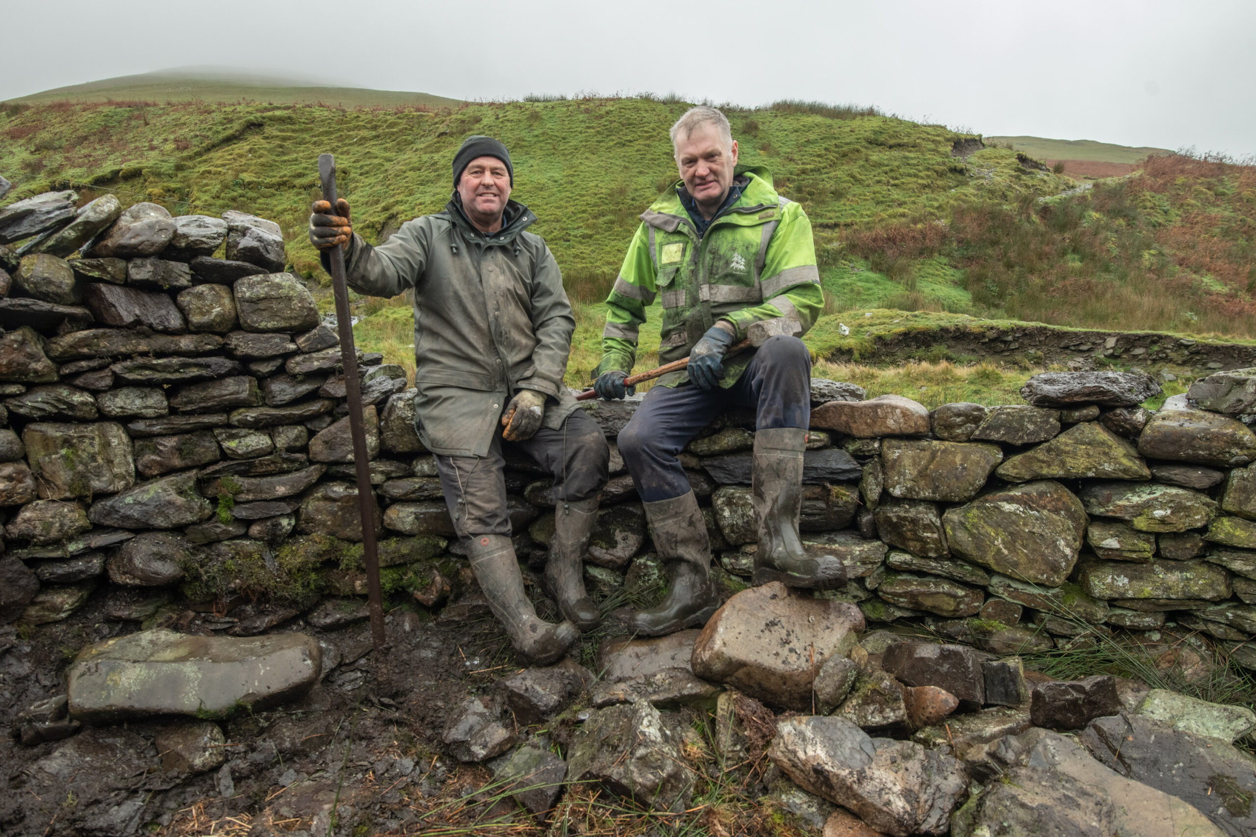 Two men sit on a dry-stone wall. They have been repairing a sheep fold on Brant Fell Common.