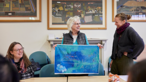 A woman holds up a fabric that says 'hej'