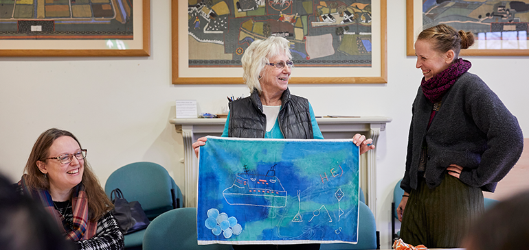 A woman holds up a fabric that says 'hej'