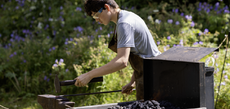 A boy blacksmithing at MERL